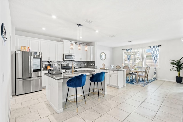 kitchen with stainless steel appliances, kitchen peninsula, dark stone counters, decorative light fixtures, and white cabinets