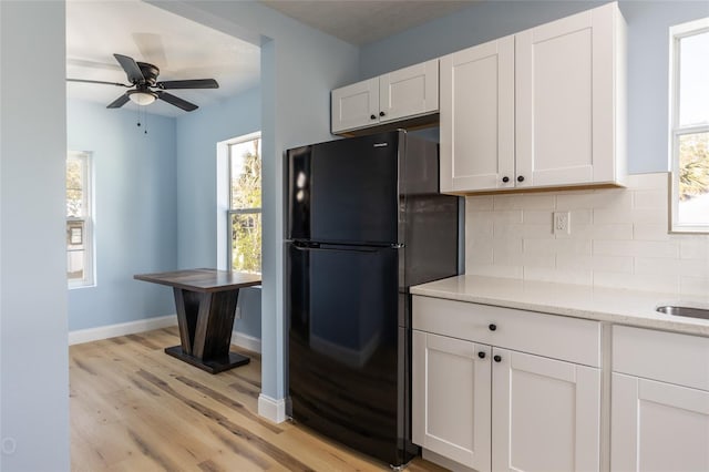 kitchen featuring light stone countertops, black fridge, decorative backsplash, white cabinets, and light wood-type flooring