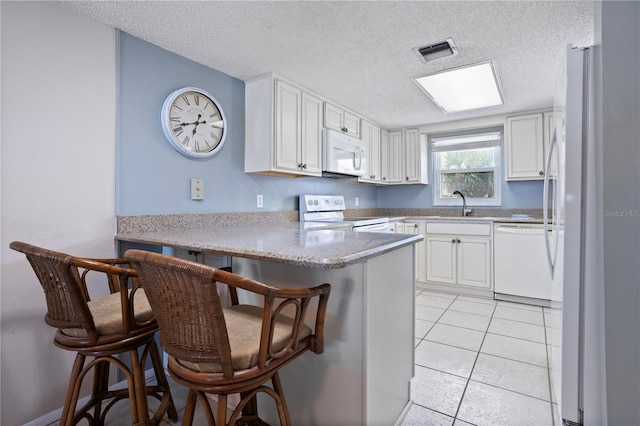 kitchen with a textured ceiling, white appliances, kitchen peninsula, and a breakfast bar area