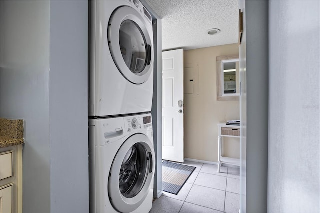 laundry area with light tile patterned floors, a textured ceiling, and stacked washer and clothes dryer