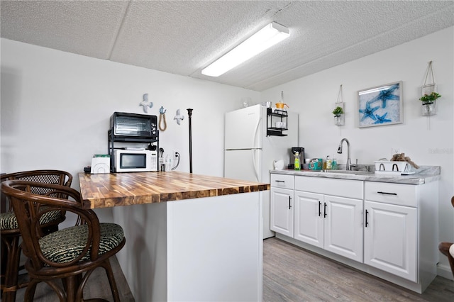 kitchen featuring a textured ceiling, sink, light hardwood / wood-style flooring, white cabinets, and butcher block counters