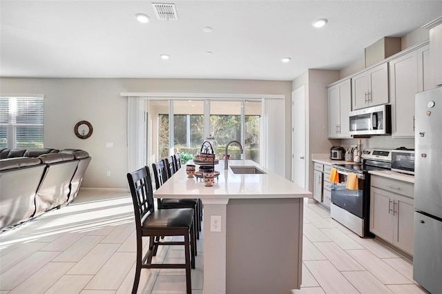 kitchen with appliances with stainless steel finishes, gray cabinetry, a breakfast bar, sink, and an island with sink