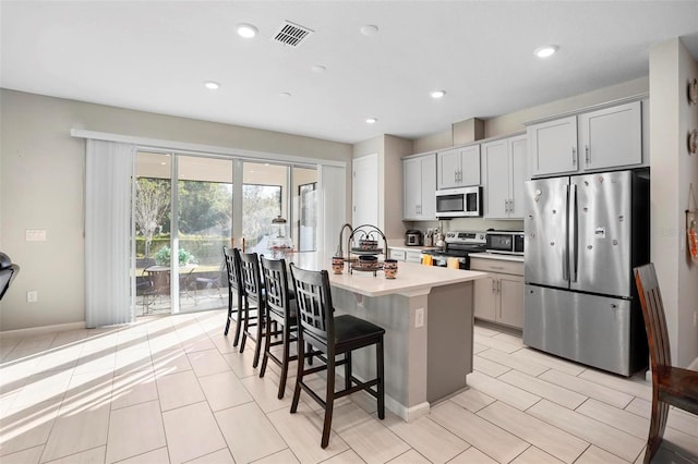 kitchen featuring a breakfast bar area, gray cabinetry, a kitchen island with sink, and stainless steel appliances