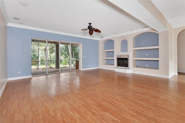 unfurnished living room featuring a high end fireplace, ceiling fan, light wood-type flooring, built in features, and ornamental molding