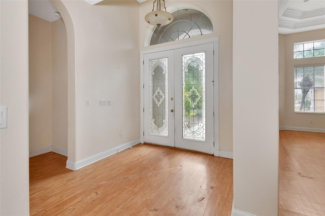 entrance foyer featuring french doors, a tray ceiling, light hardwood / wood-style flooring, and crown molding