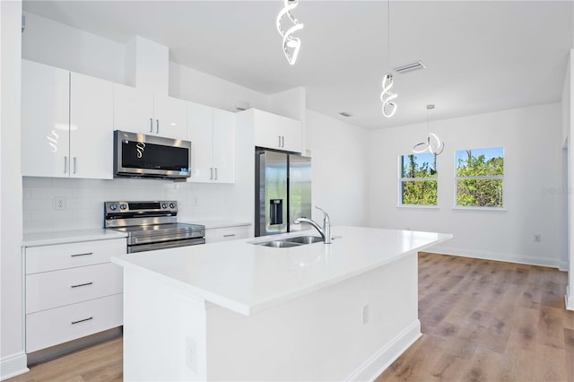 kitchen with appliances with stainless steel finishes, decorative light fixtures, a kitchen island with sink, and sink