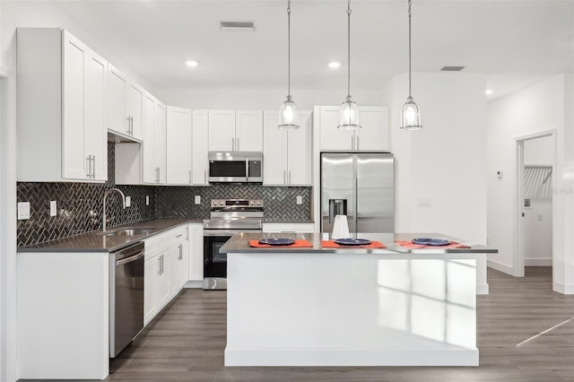 kitchen with appliances with stainless steel finishes, sink, white cabinets, a center island, and hanging light fixtures