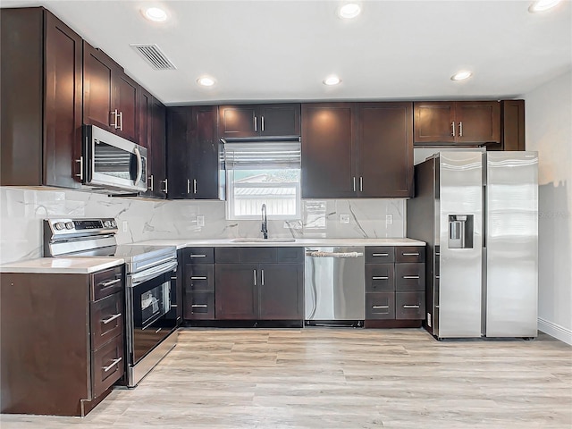 kitchen with dark brown cabinetry, sink, stainless steel appliances, decorative backsplash, and light wood-type flooring