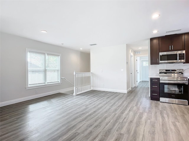 kitchen with dark brown cabinets, decorative backsplash, stainless steel appliances, and light hardwood / wood-style flooring