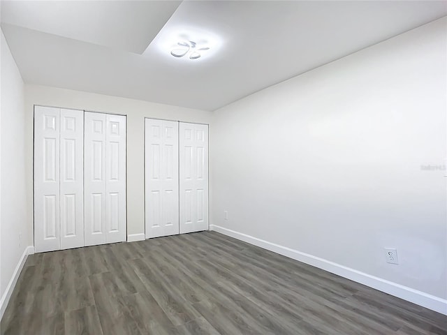 unfurnished bedroom with two closets and dark hardwood / wood-style floors