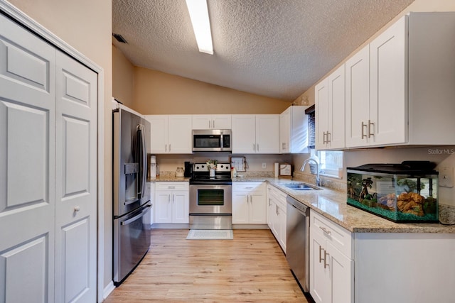 kitchen featuring white cabinetry, sink, stainless steel appliances, light hardwood / wood-style floors, and lofted ceiling