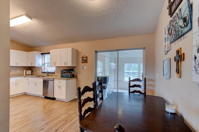 kitchen featuring white cabinets, vaulted ceiling, light hardwood / wood-style flooring, and stainless steel dishwasher