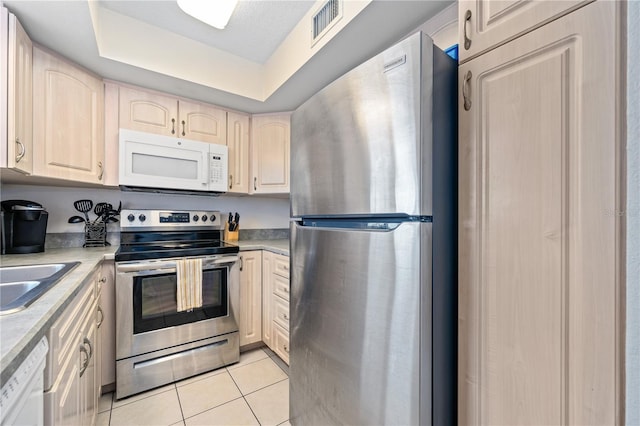 kitchen with light tile patterned floors, stainless steel appliances, a raised ceiling, and sink