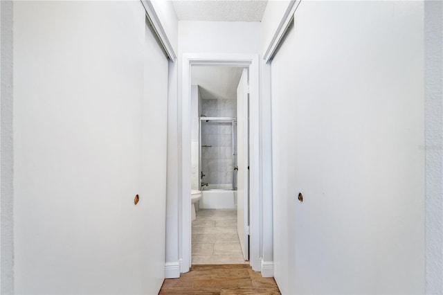 hallway with light hardwood / wood-style floors and a textured ceiling