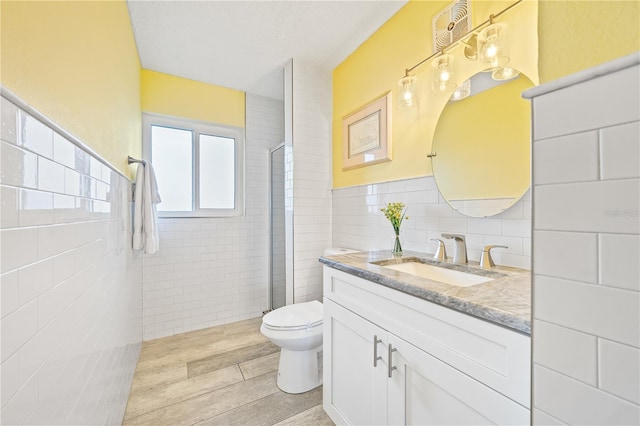 bathroom with a textured ceiling, vanity, a shower with door, tile walls, and toilet