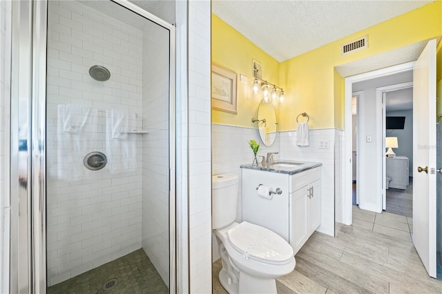 bathroom featuring walk in shower, a textured ceiling, vanity, tile walls, and toilet