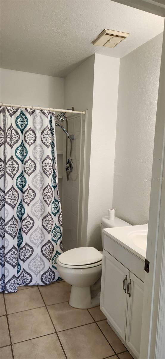 bathroom featuring vanity, tile patterned floors, a shower with curtain, toilet, and a textured ceiling