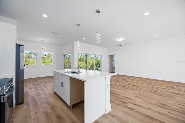 kitchen with sink, stainless steel appliances, hanging light fixtures, light hardwood / wood-style floors, and a kitchen island with sink