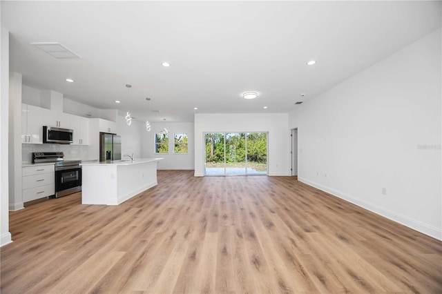 kitchen featuring light wood-type flooring, stainless steel appliances, a kitchen island with sink, pendant lighting, and white cabinetry