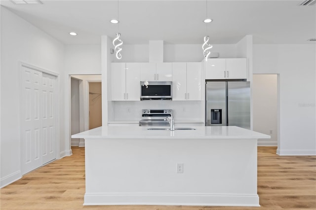 kitchen with appliances with stainless steel finishes, a kitchen island with sink, pendant lighting, light hardwood / wood-style flooring, and white cabinets