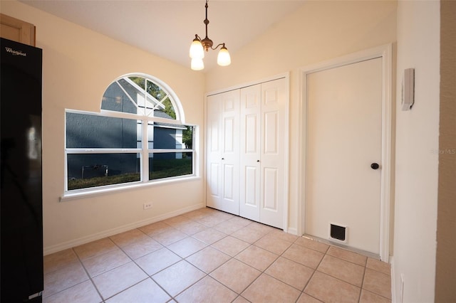 unfurnished bedroom featuring black refrigerator, light tile patterned floors, a chandelier, a closet, and lofted ceiling