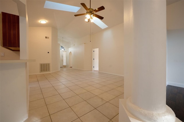 unfurnished living room with ceiling fan, vaulted ceiling with skylight, and light tile patterned flooring