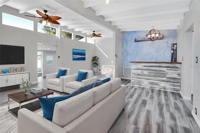 living room with beamed ceiling, light hardwood / wood-style floors, a towering ceiling, and a chandelier