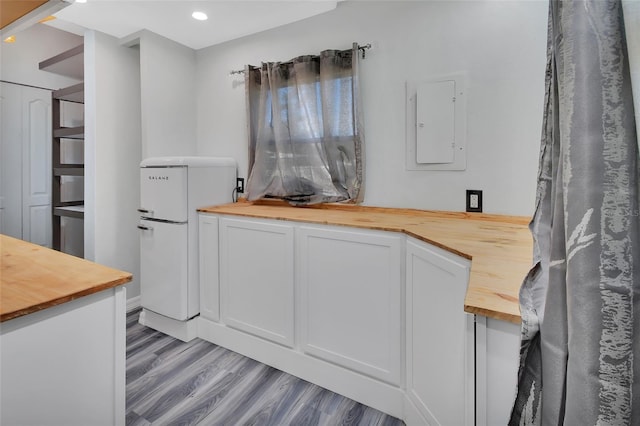 kitchen with butcher block countertops, electric panel, white fridge, light hardwood / wood-style floors, and white cabinets