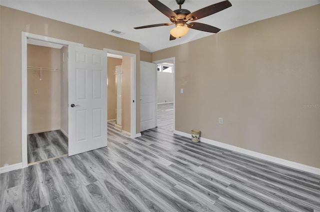 unfurnished bedroom featuring a spacious closet, ceiling fan, light wood-type flooring, and a closet