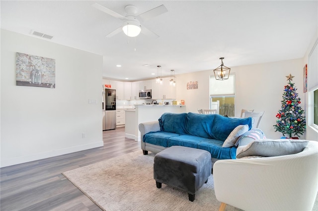 living room with ceiling fan with notable chandelier and light hardwood / wood-style flooring