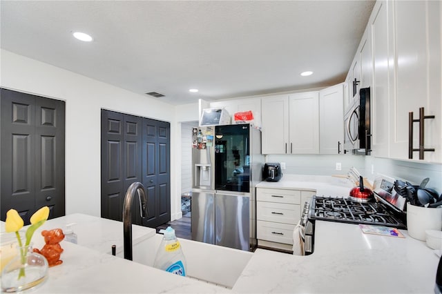 kitchen with light stone countertops, appliances with stainless steel finishes, a textured ceiling, sink, and white cabinets