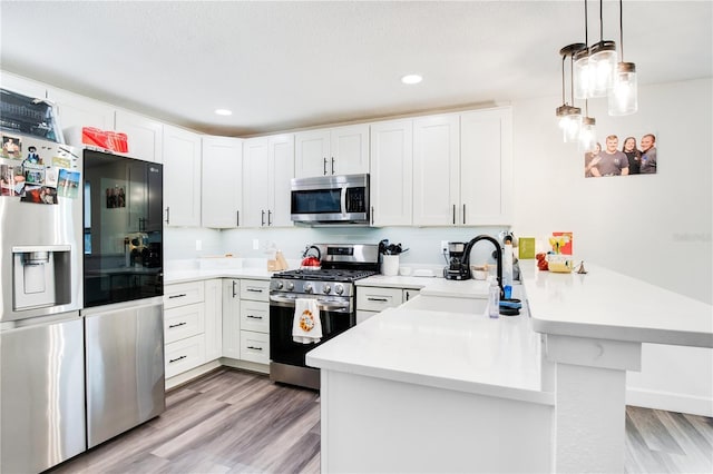 kitchen featuring white cabinets, decorative light fixtures, kitchen peninsula, and stainless steel appliances