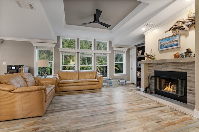 living room featuring a tile fireplace, ornamental molding, ceiling fan, a raised ceiling, and light hardwood / wood-style flooring