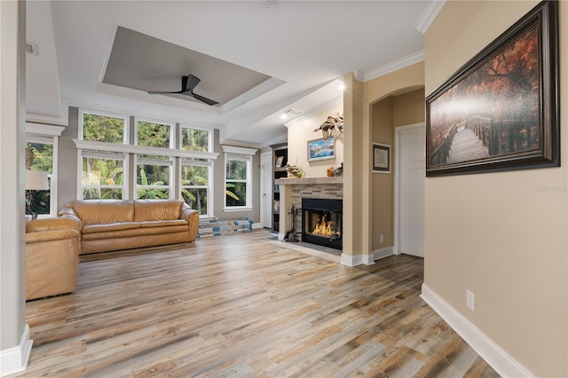 unfurnished living room with ceiling fan, a tray ceiling, a stone fireplace, and light hardwood / wood-style flooring