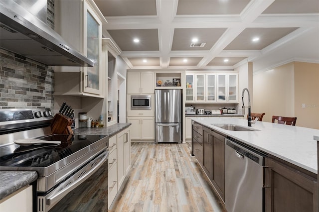 kitchen with stainless steel appliances, a sink, open shelves, light wood-style floors, and wall chimney range hood