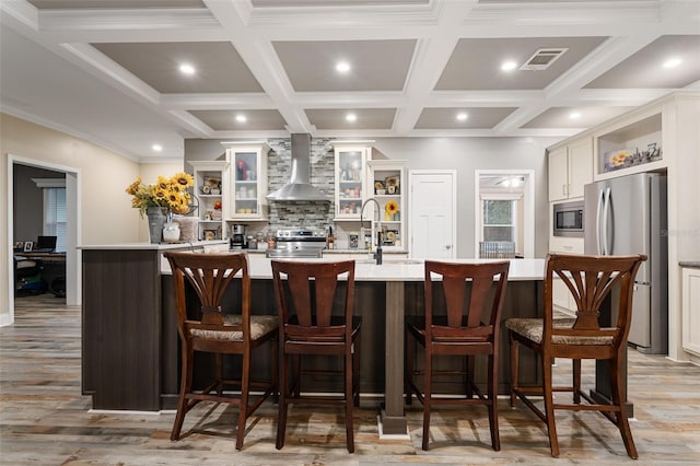 bar featuring visible vents, appliances with stainless steel finishes, a sink, wall chimney range hood, and backsplash