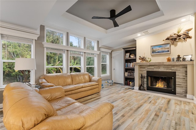 living area featuring plenty of natural light, a tiled fireplace, crown molding, and a raised ceiling