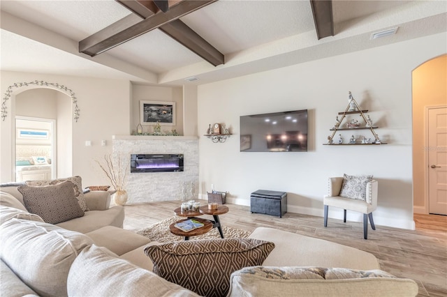 living room with a fireplace, a textured ceiling, light hardwood / wood-style flooring, and beamed ceiling