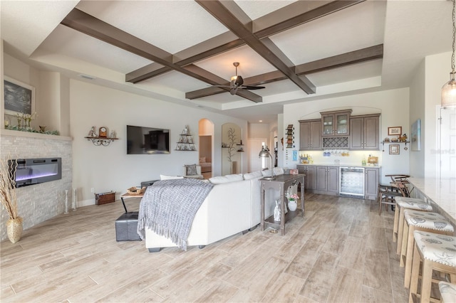 living room with ceiling fan, coffered ceiling, a stone fireplace, beamed ceiling, and light hardwood / wood-style floors