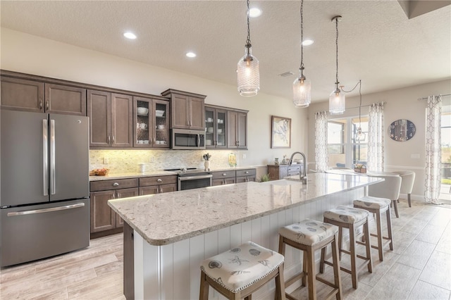 kitchen featuring a breakfast bar, a large island with sink, hanging light fixtures, light stone countertops, and stainless steel appliances