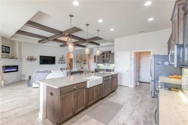 kitchen featuring sink, an island with sink, decorative light fixtures, light hardwood / wood-style floors, and stainless steel appliances