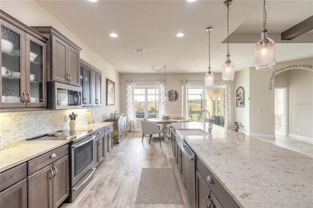 kitchen featuring dark brown cabinetry, hanging light fixtures, stainless steel appliances, light hardwood / wood-style floors, and a textured ceiling