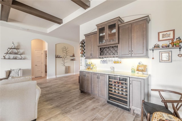 bar featuring beam ceiling, dark brown cabinetry, light hardwood / wood-style floors, and wine cooler