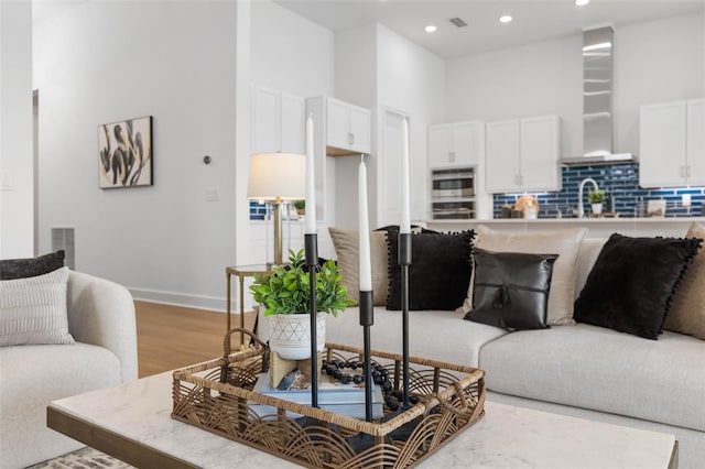 living room featuring light wood-type flooring, sink, and a high ceiling