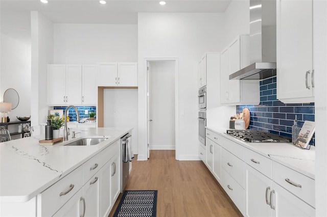 kitchen featuring light wood-type flooring, white cabinetry, wall chimney exhaust hood, and sink