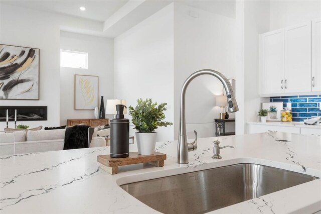 interior details with light stone countertops, backsplash, white cabinetry, and sink