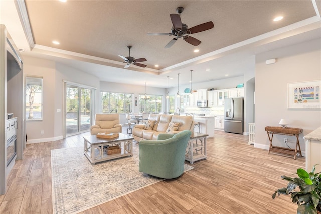 living room featuring ceiling fan, crown molding, light hardwood / wood-style flooring, and a tray ceiling