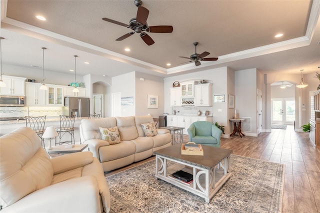 living room featuring hardwood / wood-style floors, french doors, ceiling fan, ornamental molding, and a tray ceiling