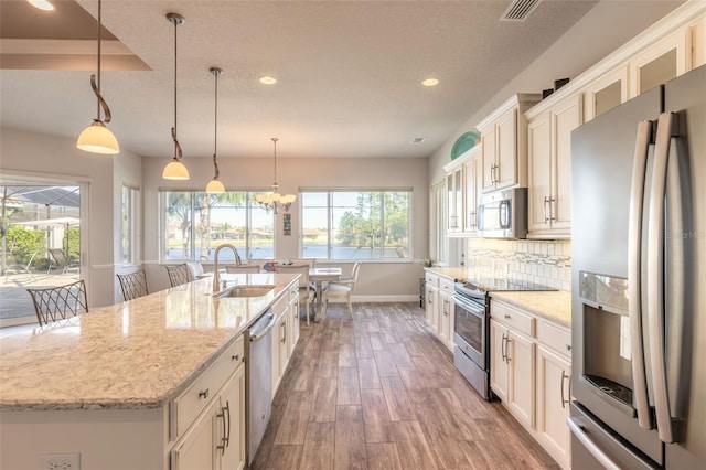 kitchen with a center island with sink, sink, hardwood / wood-style flooring, appliances with stainless steel finishes, and decorative light fixtures