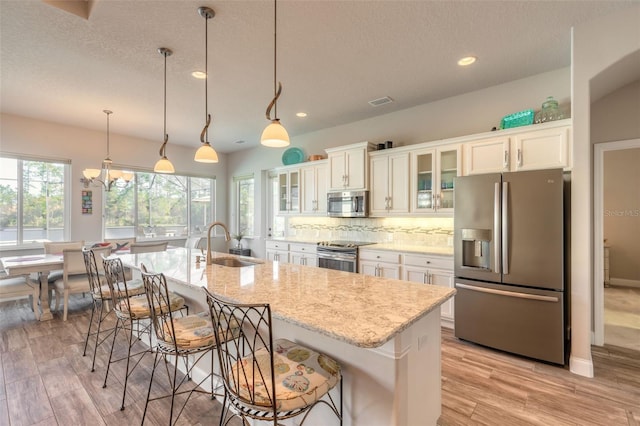 kitchen with light hardwood / wood-style floors, sink, stainless steel appliances, and an island with sink